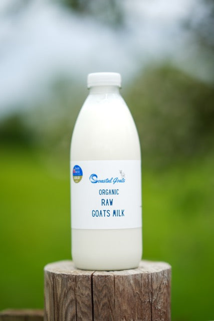 Bottle of organic raw goats milk on a wooden block with a blurred green background
